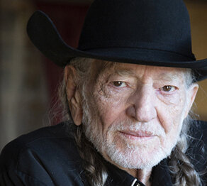 Willie Nelson in back shirt and hat looking thoughtful