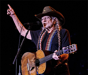Willie Nelson playing guitar to a crowd pointing at audience